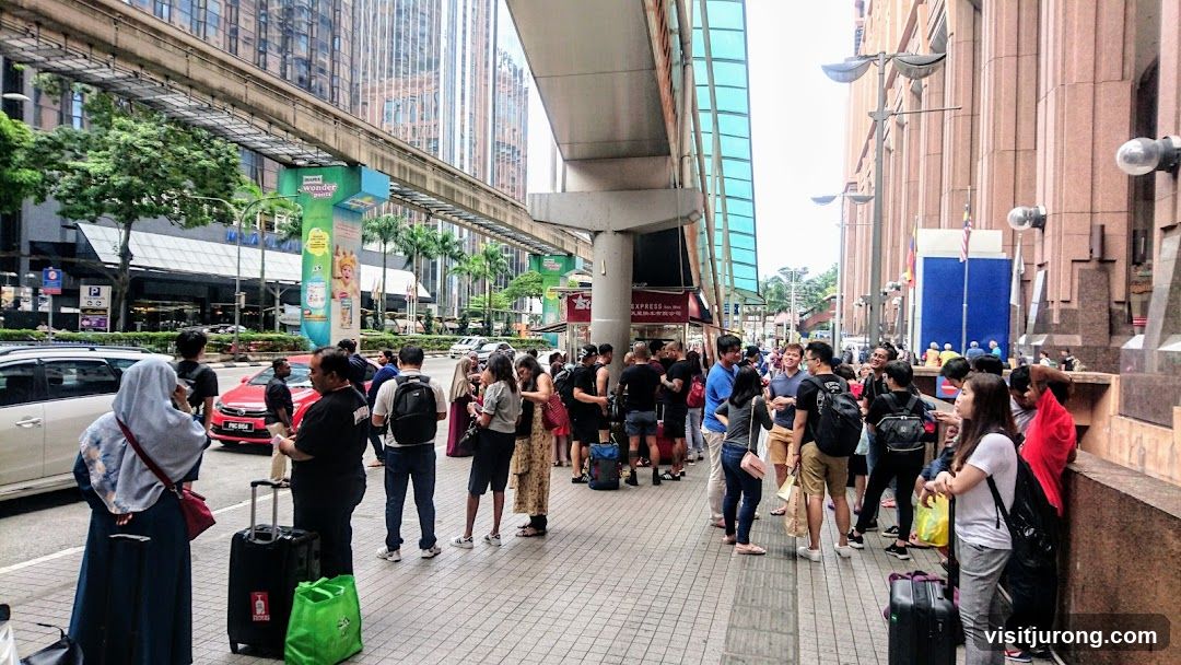 People waiting on a sidewalk under a monorail track
