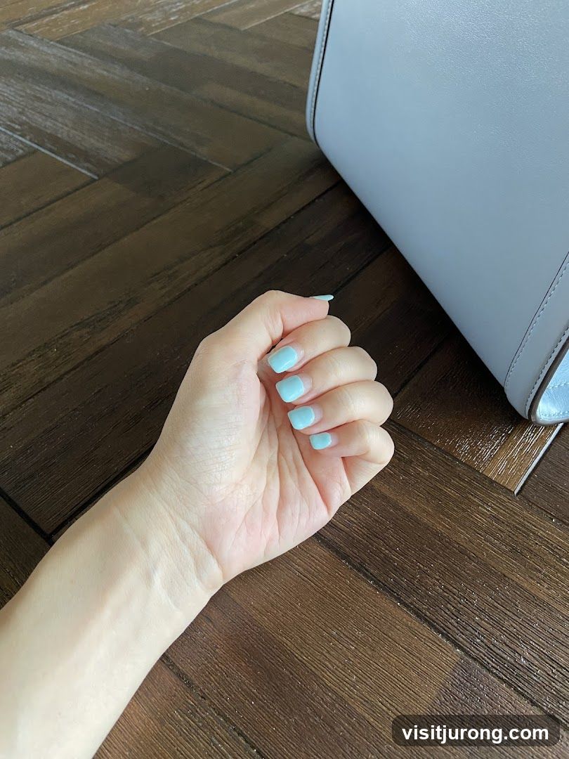 Hand with light blue nails resting on wooden floor next to a light blue bag