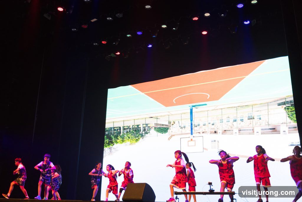 Children performing on stage with a basketball court backdrop