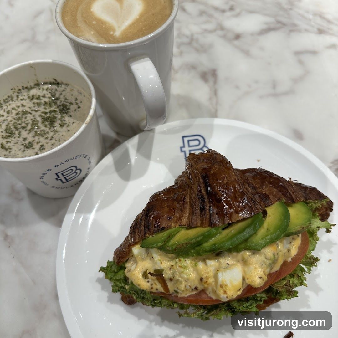 Croissant sandwich with avocado and egg salad, soup, and latte