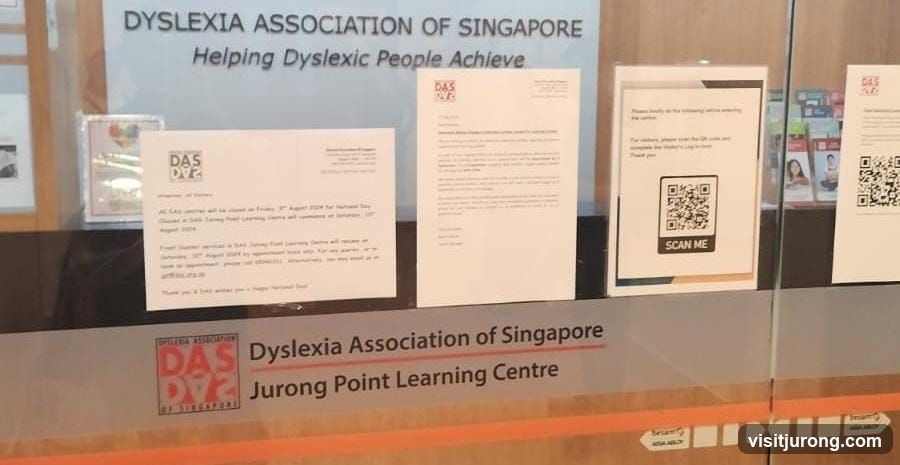 The image shows the entrance to the Dyslexia Association of Singapore, Jurong Point Learning Centre. There are several notices posted on the glass door, including information about closures and a QR code for visitors to scan. The main signage for the association is visible on the glass.