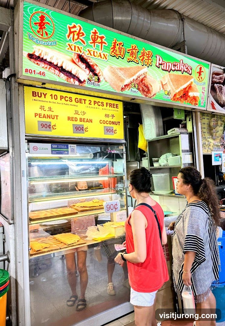 A stall selling vegetarian pancakes with various fillings. The stall has a large sign with images of the pancakes and the name of the stall. Below the sign is a price list and a promotion for buying 10 pieces. Two customers are seen at the counter.