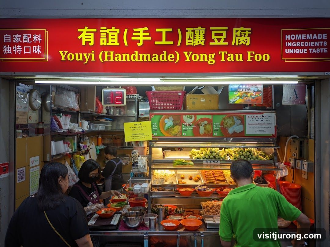 A food stall with a red sign displaying the name of the stall in Chinese and English, along with "Homemade Ingredients Unique Taste". Below the sign, various food items are displayed in refrigerated cases. People are seen ordering and preparing food.