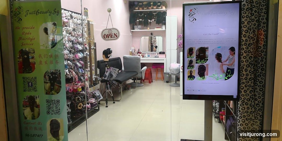 The image shows the storefront of a beauty salon. A green banner on the left advertises "Updo Hairstyle Service" and provides contact information. Inside, shelves are stocked with hair accessories and wigs. A vanity area with chairs and a mirror is visible. A digital display shows images of hairstyles and the salon's name. An "OPEN" sign hangs on the door.