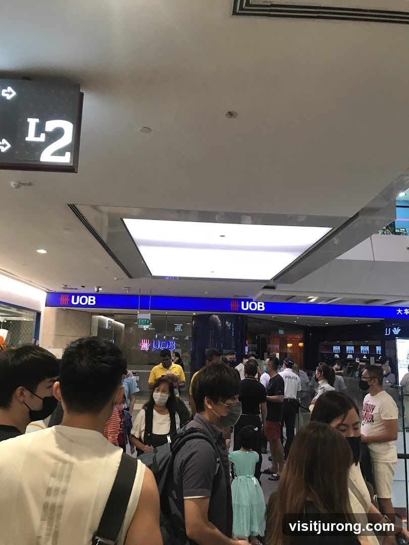 A crowd of people are gathered in front of a UOB bank. The bank's signage is visible above the entrance. There is also a sign indicating 'L2' for Level 2.